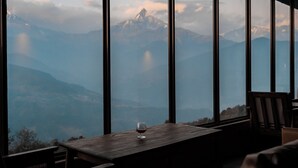 Une table avec un verre de vin et une vue sur les montagnes, visible à travers de grandes fenêtres.