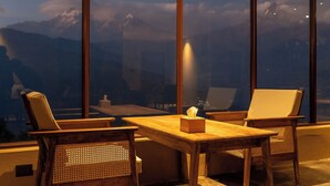 Une table en bois, deux chaises, une boîte de mouchoirs et une vue sur les montagnes par de grandes fenêtres.