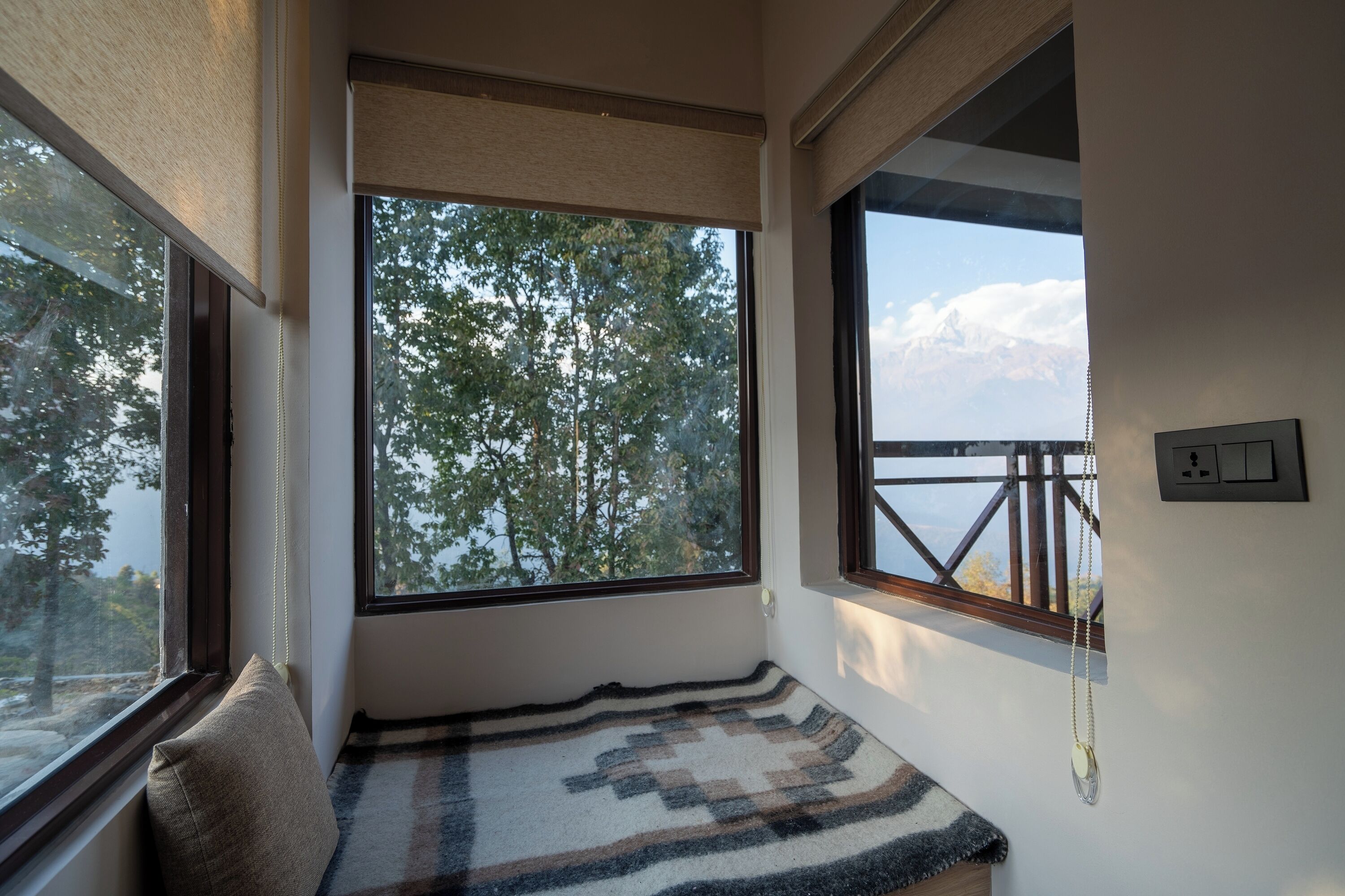 Ein Zimmer mit einem großen Fenster und Blick auf Bäume und ein fernes Gebirge.