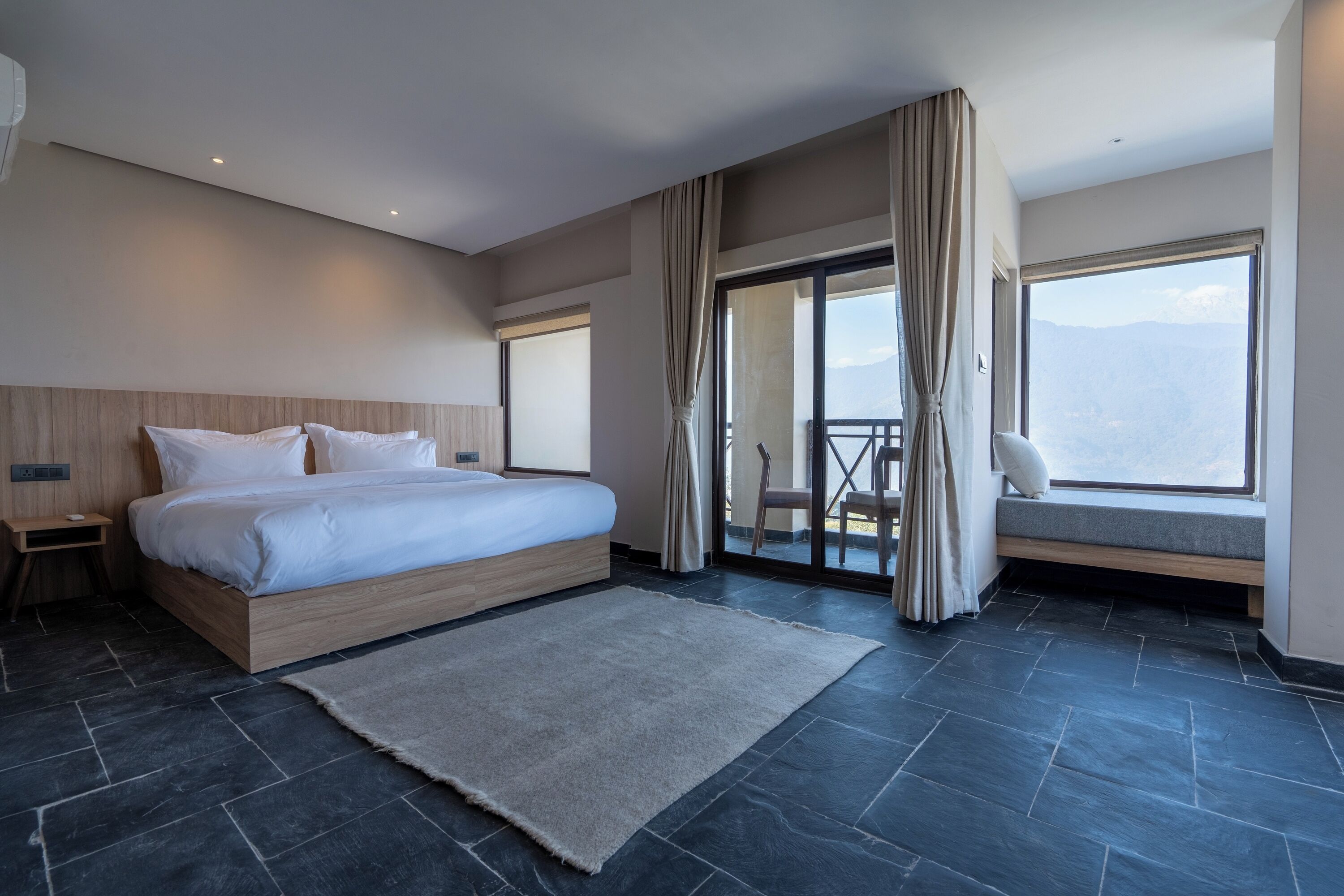 Quarto de hotel moderno com uma cama grande, uma varanda com vista e uma porta de correr de vidro.