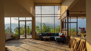 Un vaste espace de vie avec une grande fenêtre donnant sur les montagnes, un canapé, une table basse et un sol en pierre.
