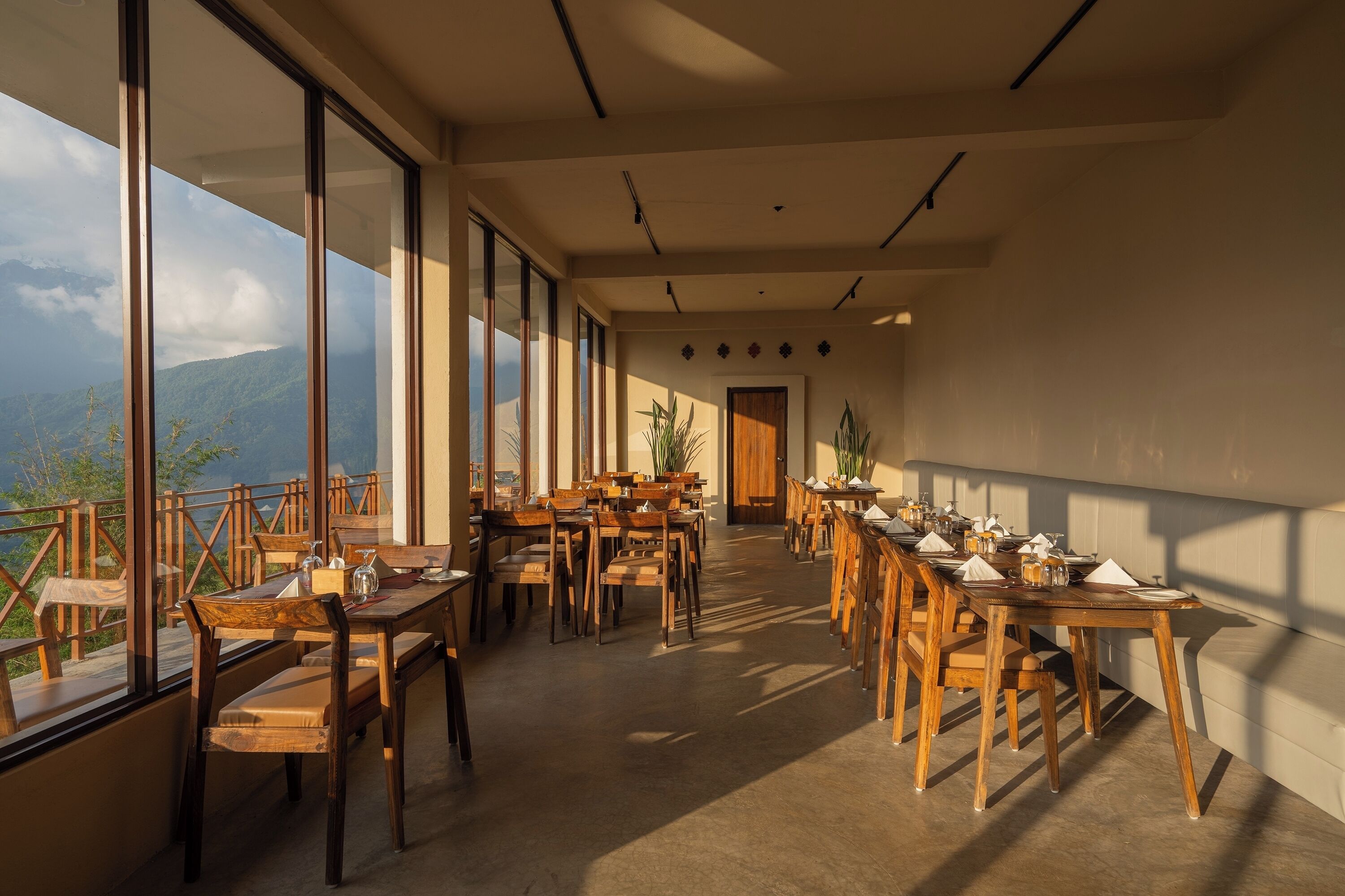 A spacious dining area with wooden tables and chairs, large windows offering mountain views, and a modern interior design.