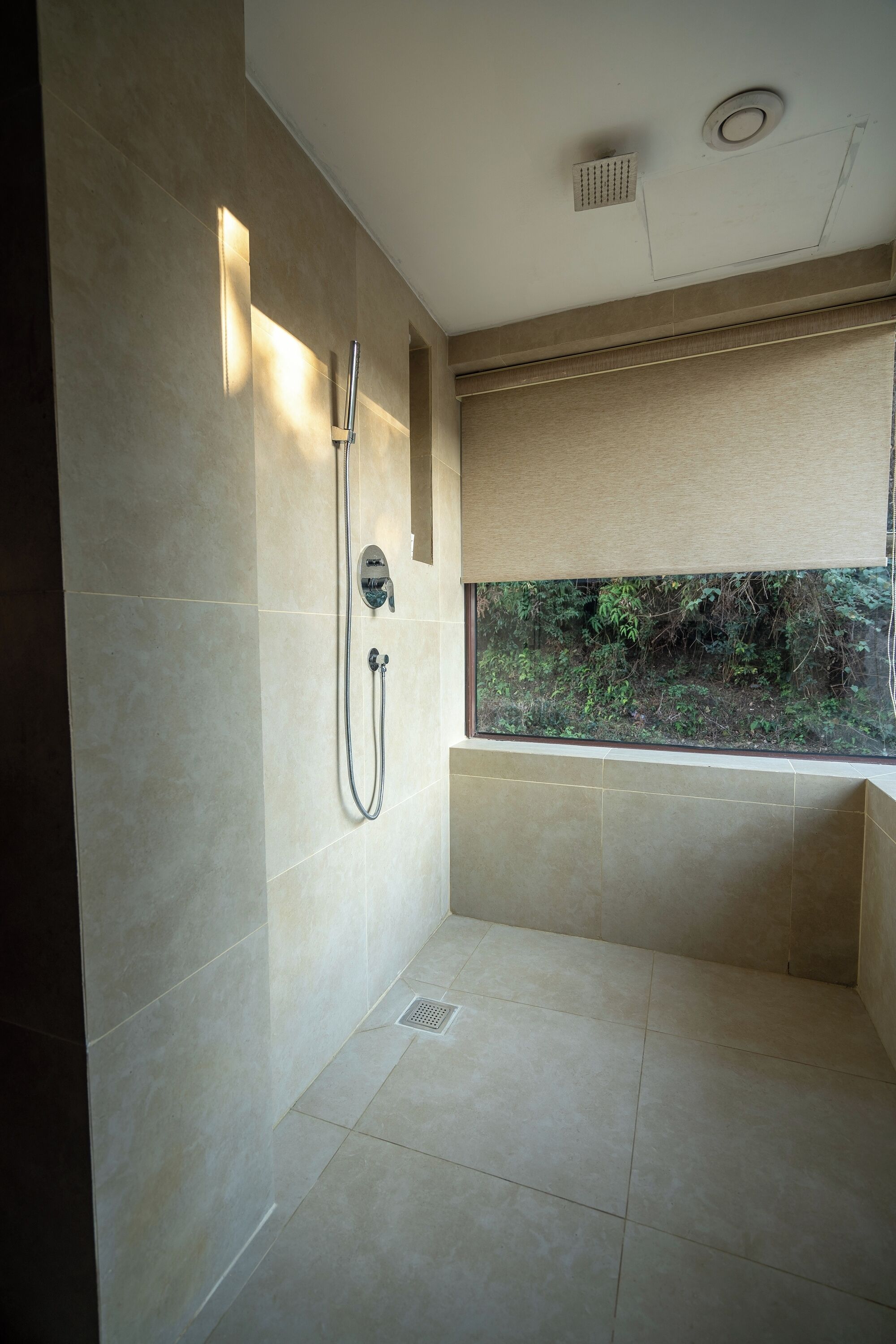 A modern bathroom with a shower, a window with a view of greenery, and a ceiling light.