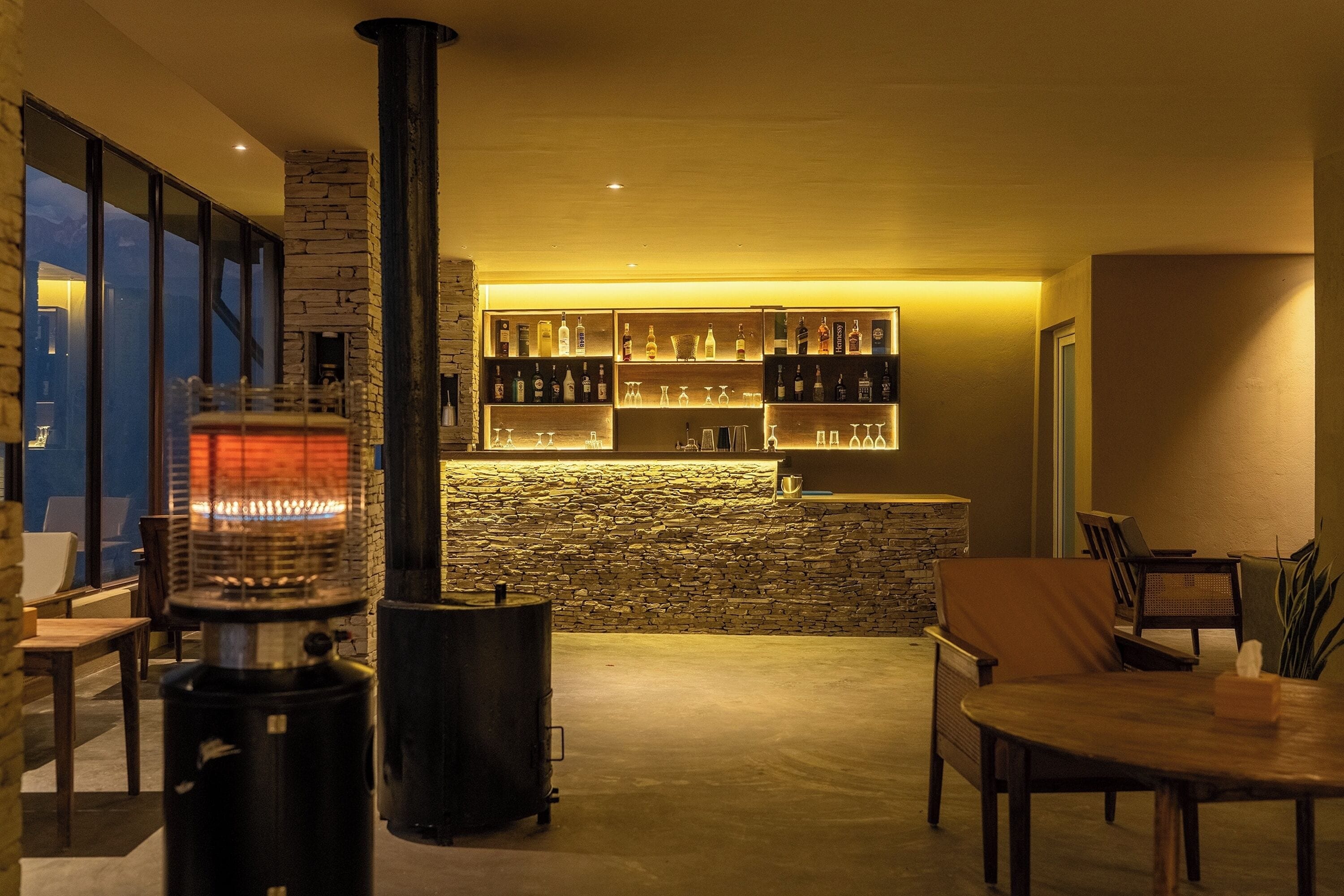 A cozy living area with a fireplace, a stone wall, and a bar with shelves of bottles.