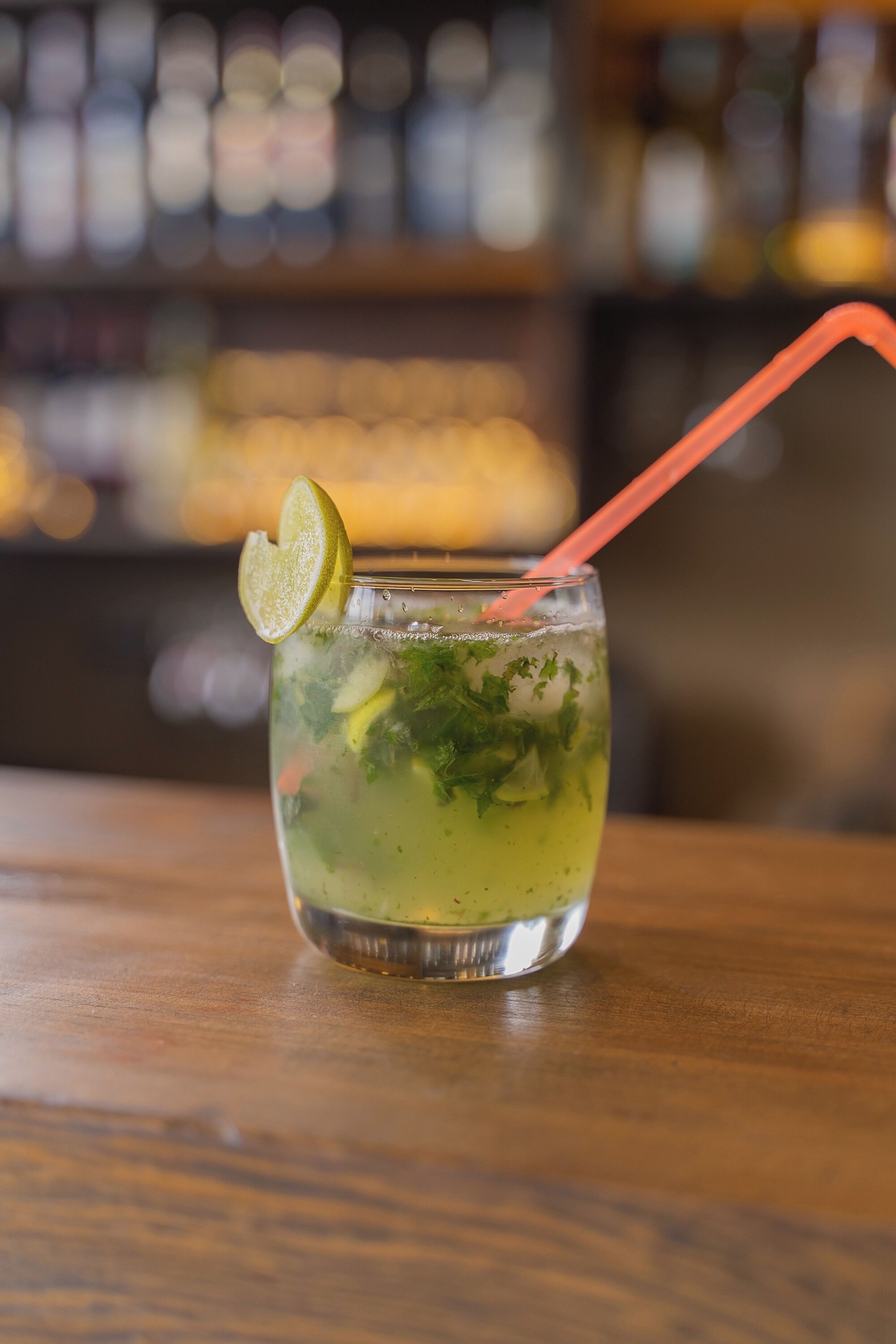 Ein Glas grüner Cocktail mit Limettenscheibe und Strohhalm auf einer Holztischplatte.