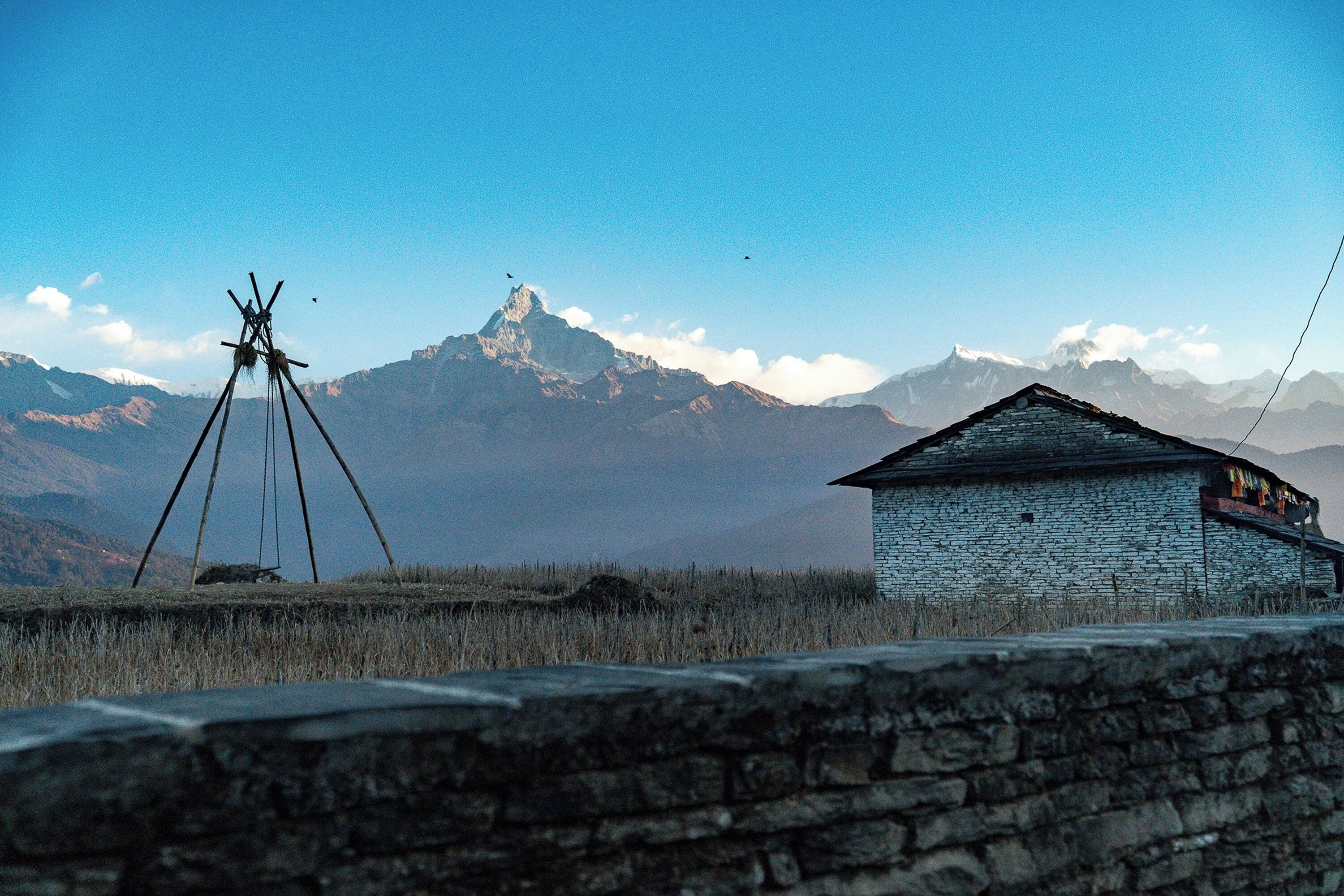 A stone building with a sloped roof, a small balcony, and a clear view of a mountain range in the background.