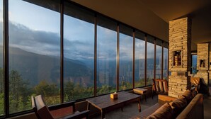 Une pièce spacieuse dotée de grandes fenêtres offrant une vue sur les montagnes, d’une cheminée en pierre et de sièges confortables.