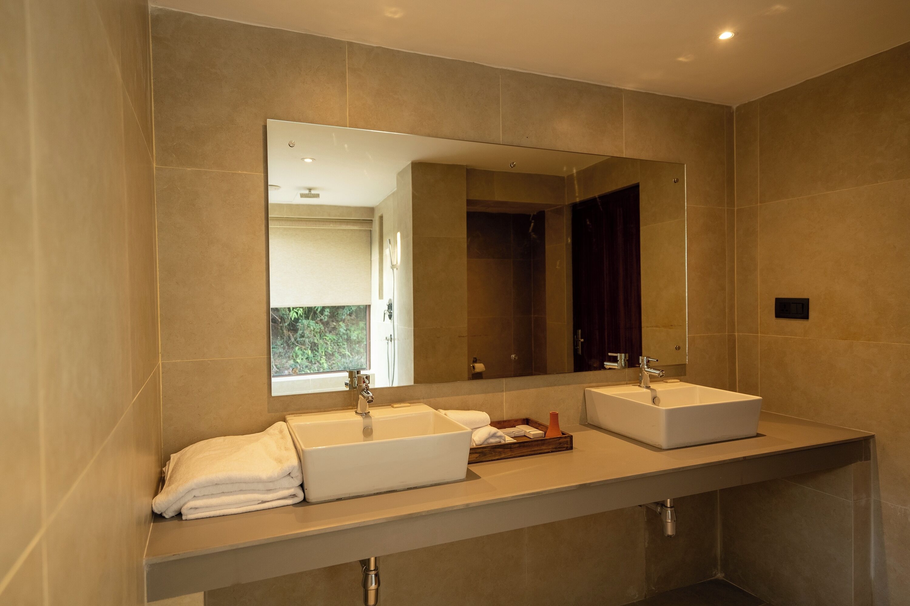 A modern bathroom with two sinks, a large mirror, and a view of the outside.