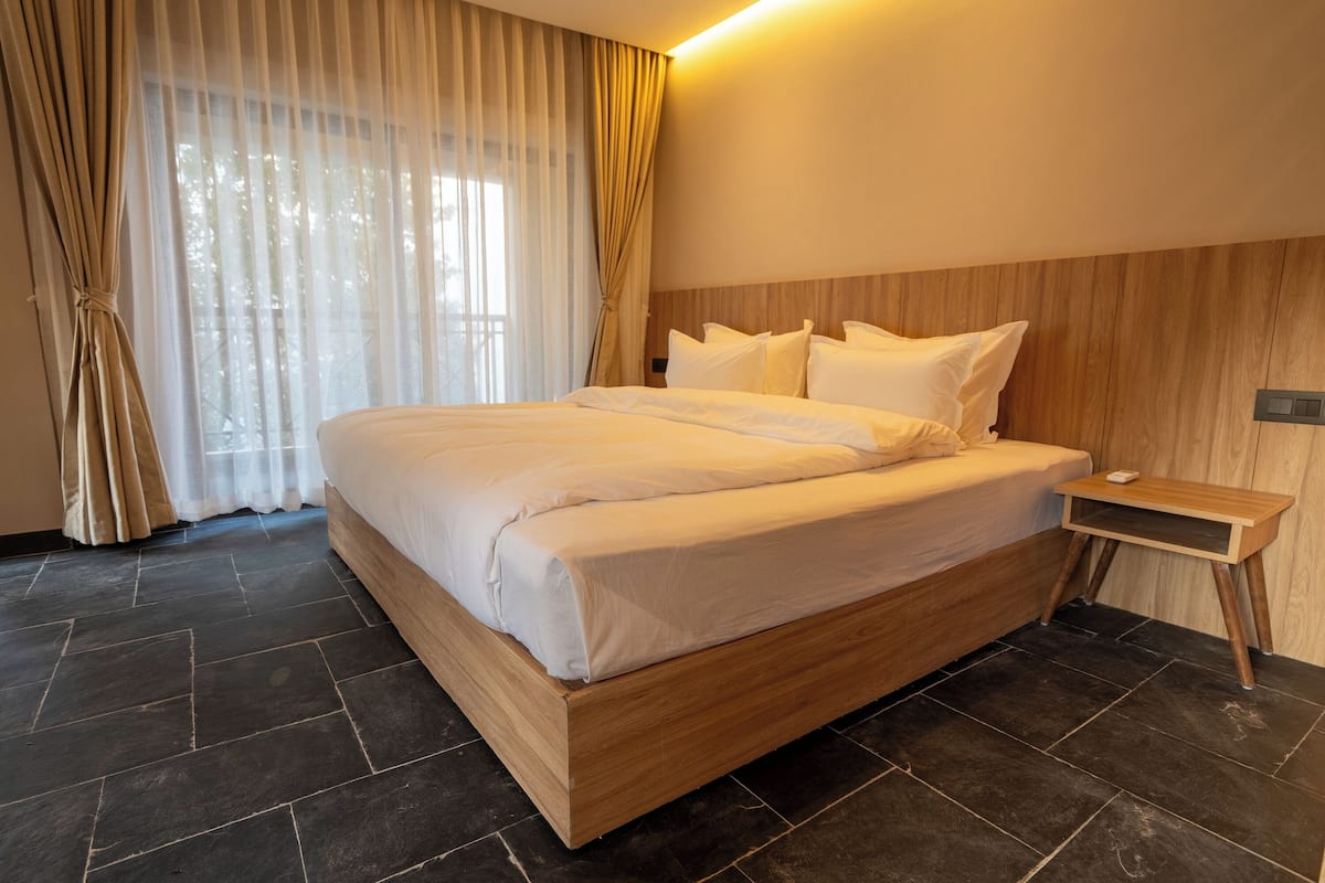 A modern hotel room with a large bed, wooden headboard, and a nightstand.