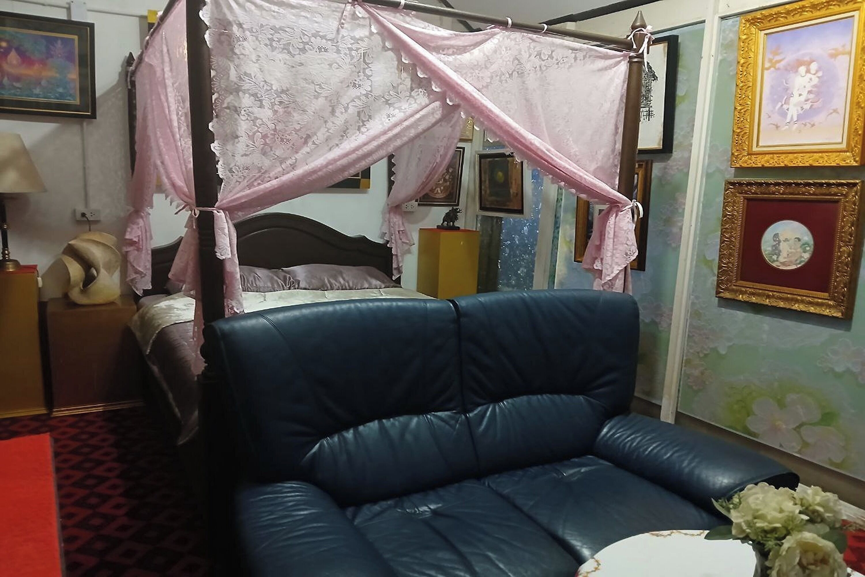 Una habitación con una cama de dos columnas, un sofá de cuero azul y una mesita con un jarrón de flores.