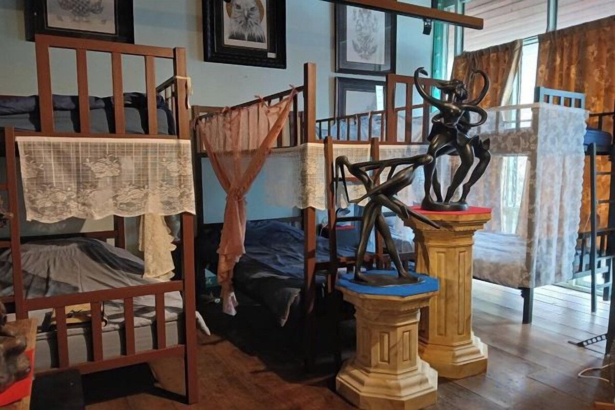 A room with a bunk bed, a wooden chair with a lace cover, and a statue on a pedestal.