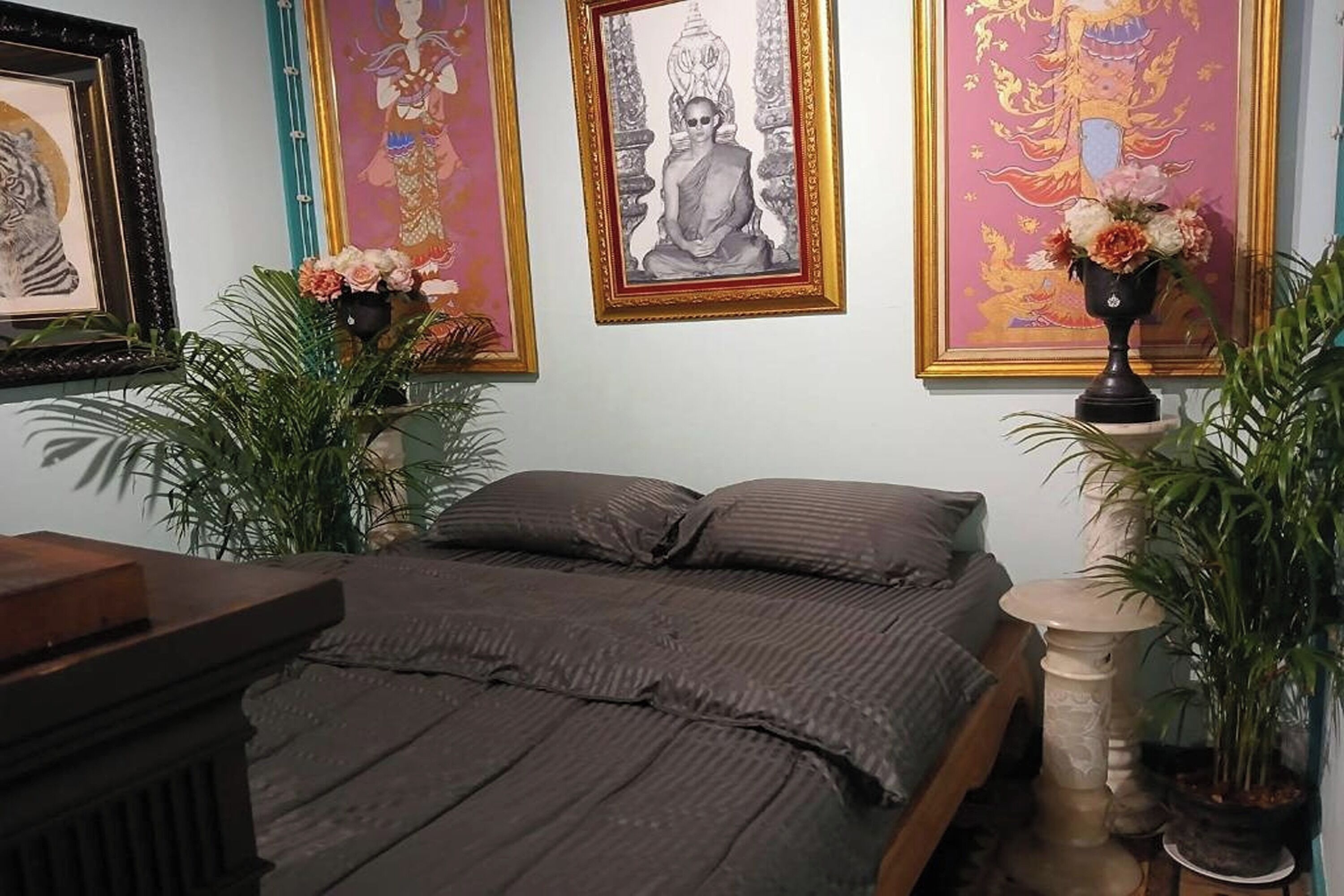 A bedroom with a bed, framed artwork, and potted plants.