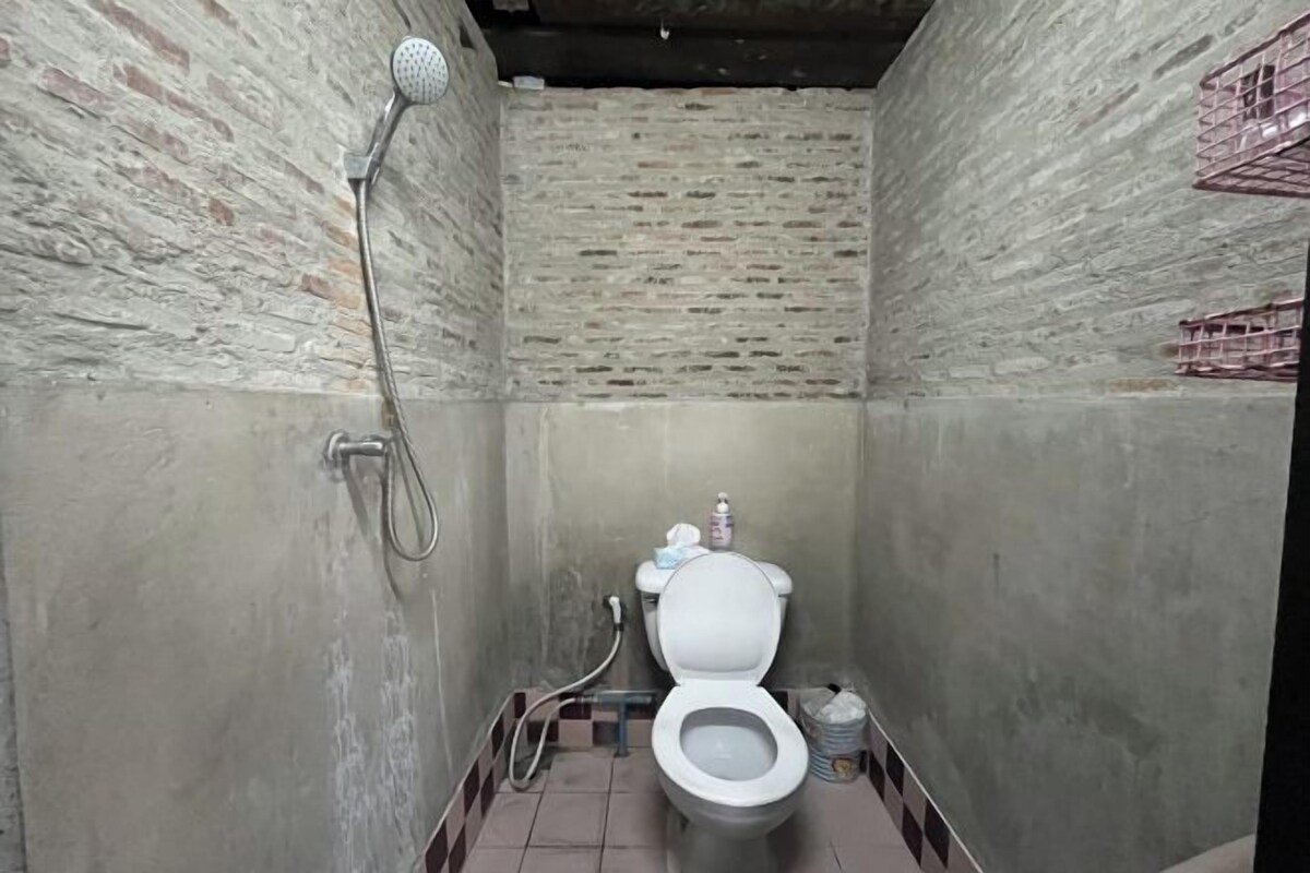 A small, enclosed bathroom with a toilet, a showerhead, and a tiled floor.