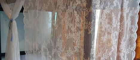 A bed with a white bedspread and lace curtains.