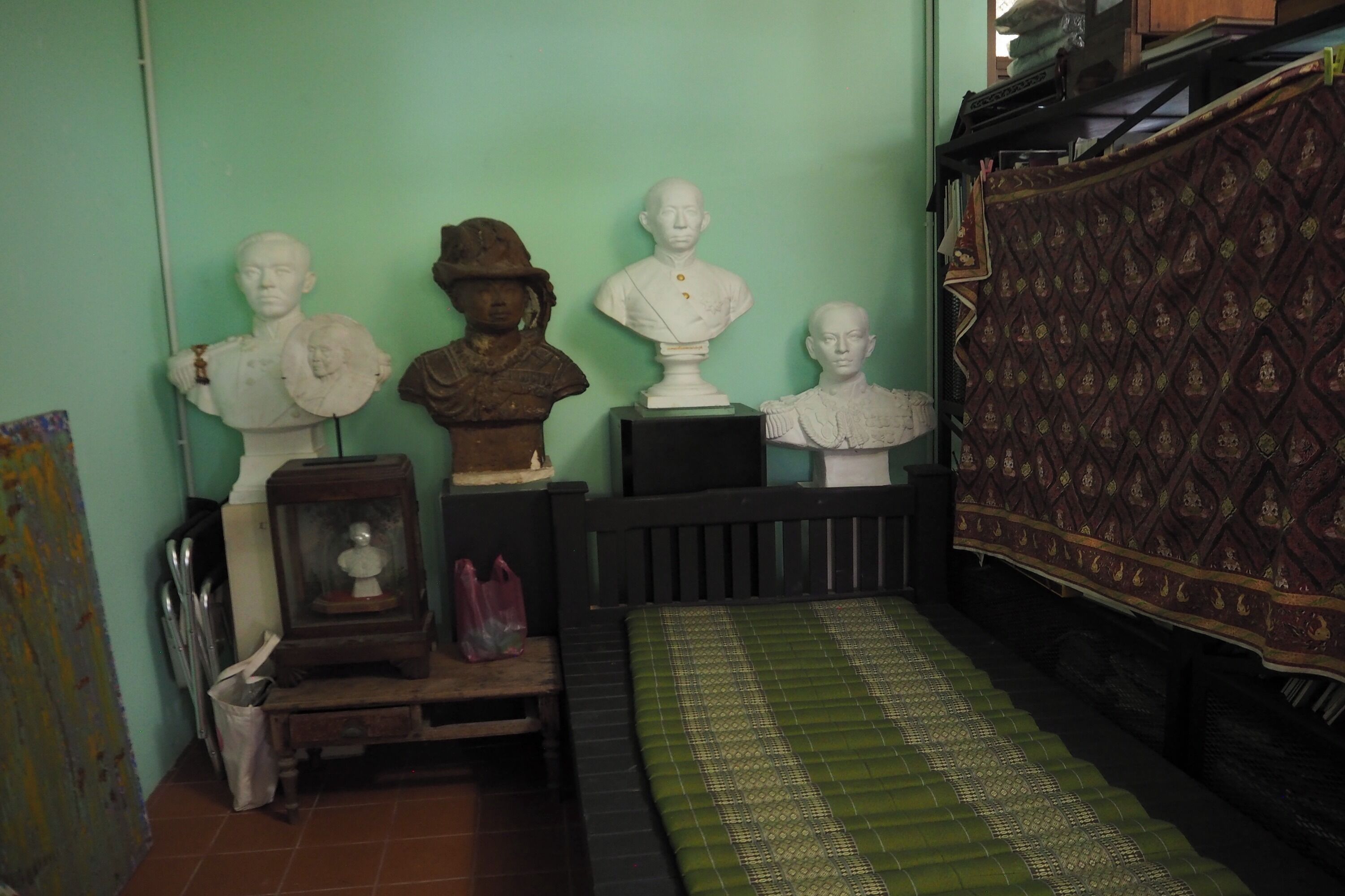 Una habitación con pared verde, colcha estampada y tres bustos en una estantería.