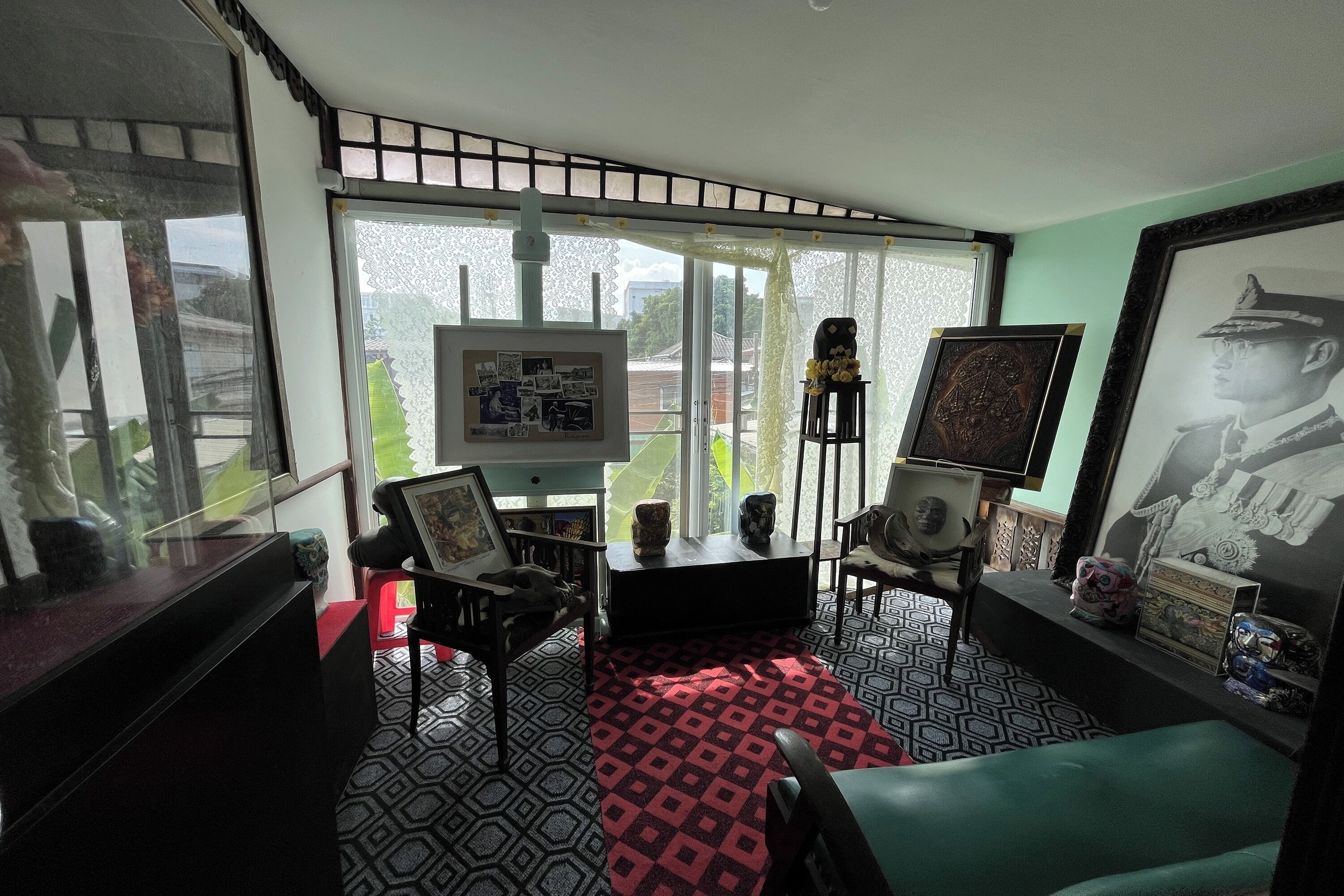 A room with a large window, a black and white patterned floor, a red and black rug, and a green sofa.