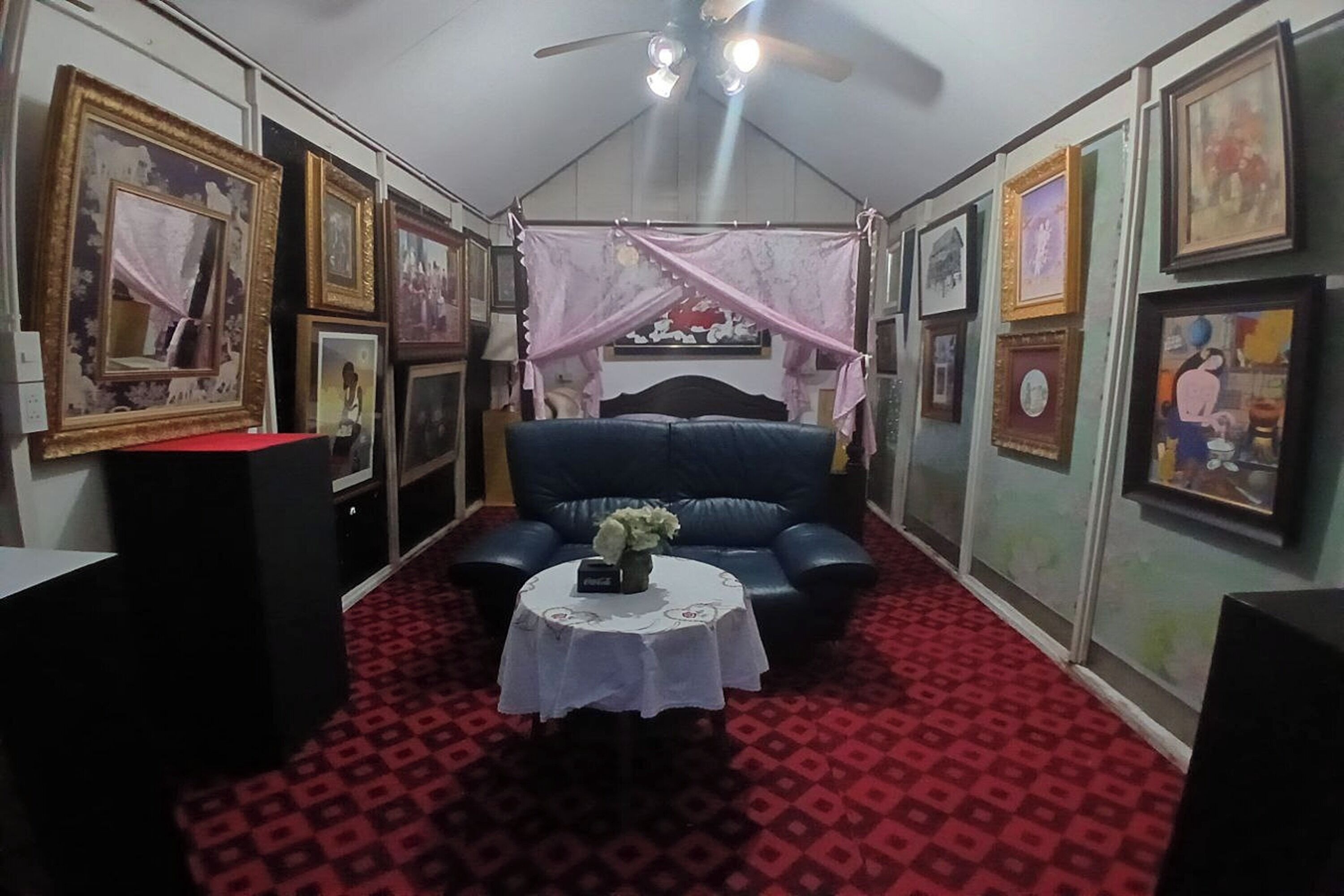 A room with a bed, a table with a vase, and framed pictures on the walls.