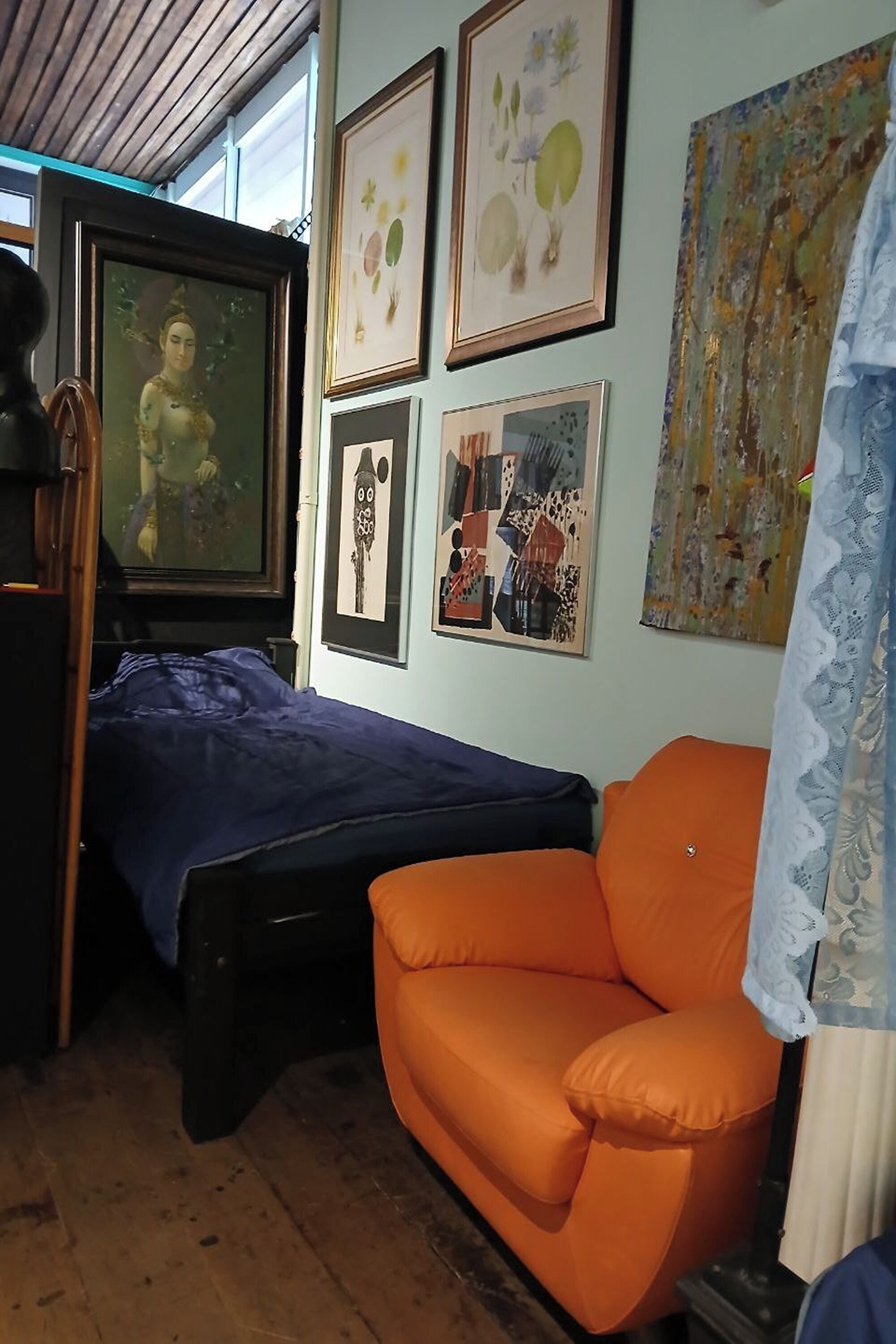 Une pièce comprenant un lit, une chaise et des œuvres d’art accrochées aux murs.