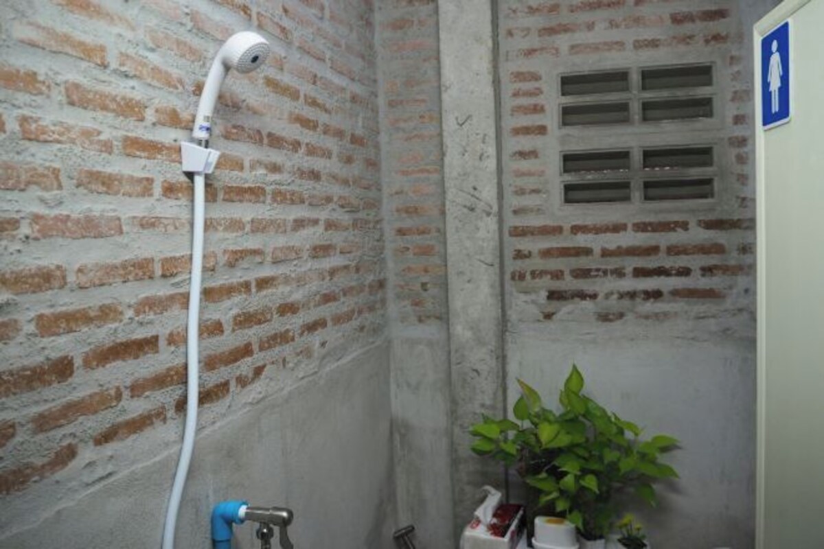 A narrow, brick-walled bathroom with a shower, a hand dryer, and a potted plant.