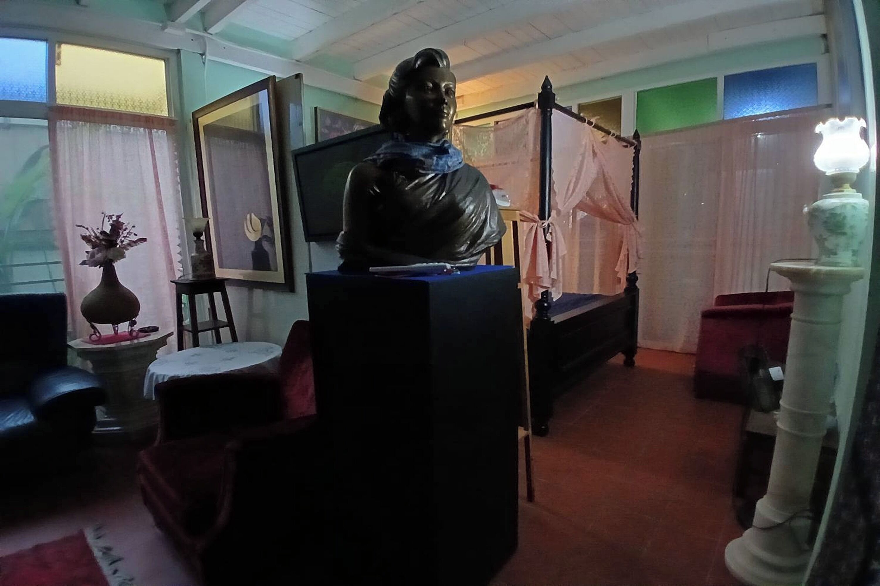 A room with a bed, a statue, a television, and a vase with flowers.
