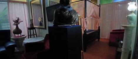 A room with a bed, a statue, a television, and a vase with flowers.