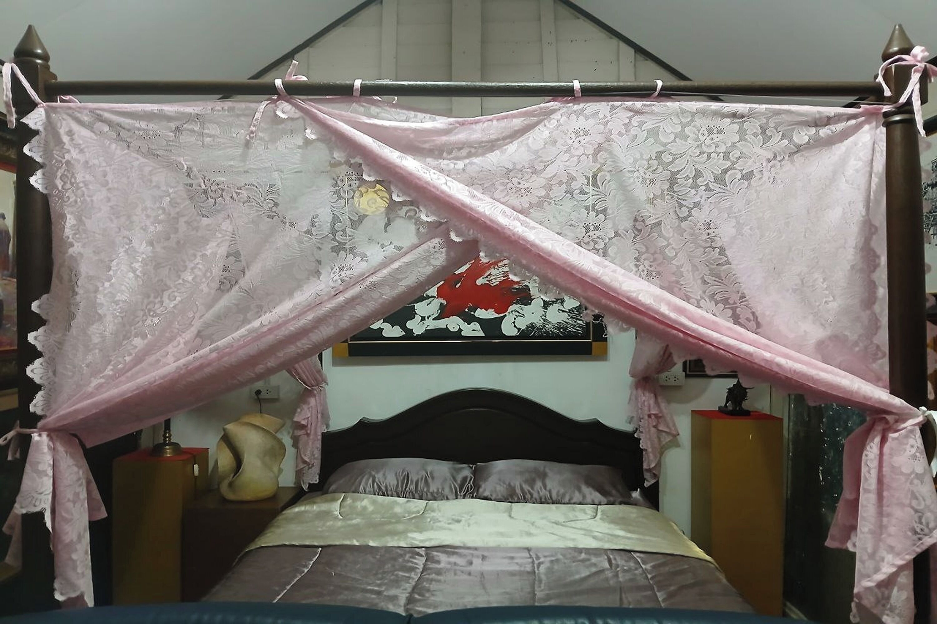 Een slaapkamer met een bed onder een hemelbed, een hoofdbord, nachtkastjes en een wanddecoratie.