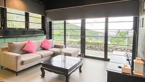 Ein modernes Wohnzimmer mit einem beigefarbenen Sofa, einem Couchtisch und Blick auf eine grüne Landschaft durch große Fenster.