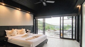 Ein modernes Schlafzimmer mit einem großen Bett, einem Deckenventilator und einem Balkon mit Blick auf Grünflächen.