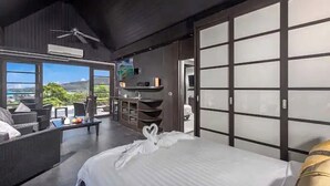 Ein modernes Hotelzimmer mit einem großen Bett, einem Balkon mit Aussicht, einer Sitzecke und einer Schiebetür.