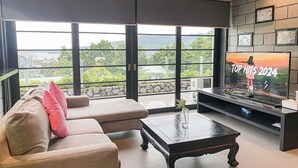 Ein modernes Wohnzimmer mit großem Fernseher, bequemen Sitzmöglichkeiten und einem Balkon mit Blick auf die Stadt.