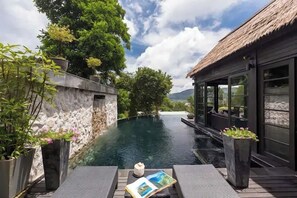 A serene pool area with a stone wall, potted plants, and a thatched-roof structure. - Jaokhun Panorama Villas, Kamala (Kamala)
