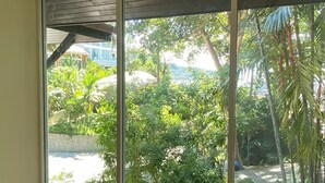 A room with a large sliding glass door leading to a garden area with tropical plants and a view of a building in the distance. - Jaokhun Panorama Villas, Patong (Patong)