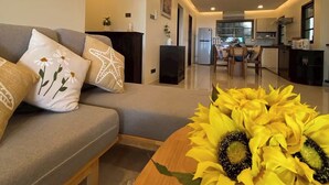 A modern living room with a sofa, a wooden coffee table with sunflowers, and a kitchen in the background. - Jaokhun Panorama Villas, Patong (Patong)