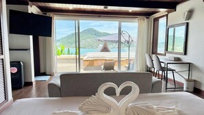 A hotel room with a bed, a desk, and a view of a mountain and lake. - Panorama Ocean Villas, Kamala (Kamala)