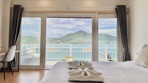 A hotel room with a large bed, a desk, and a view of a mountain and sea through a sliding door. - Panorama Ocean Villas, Kamala (Kamala)