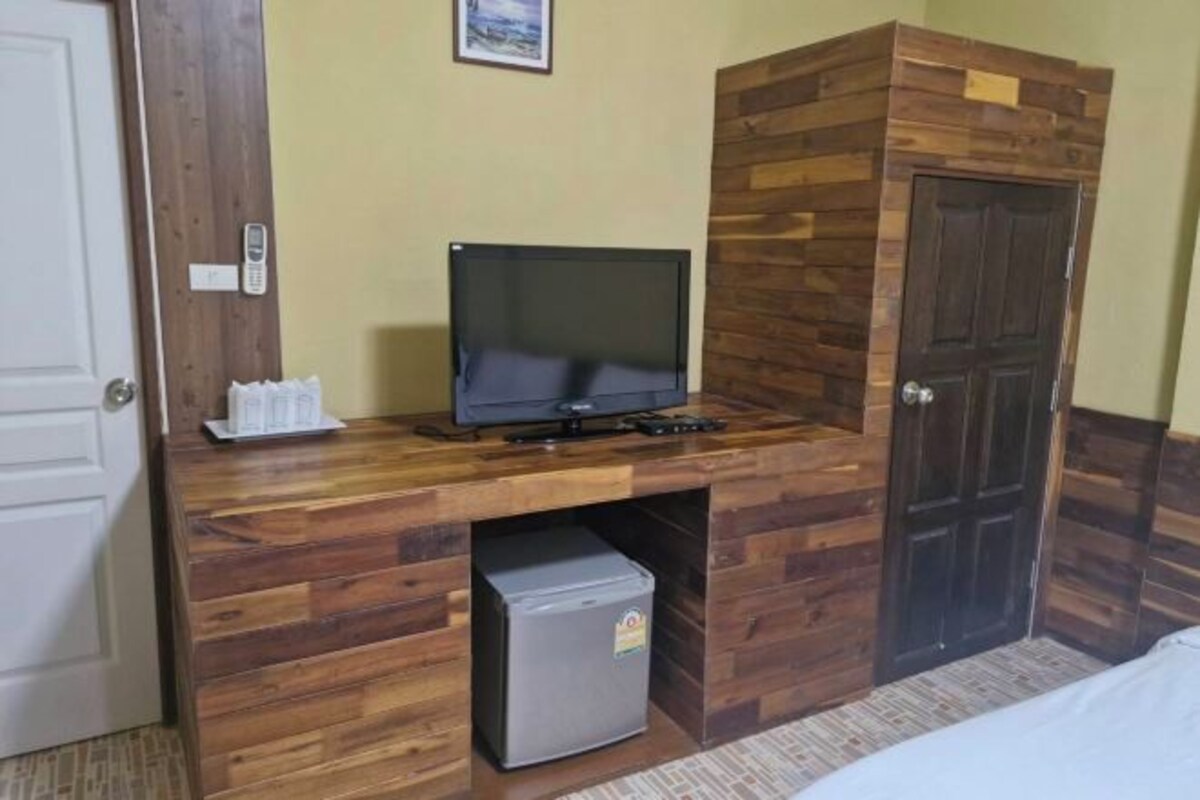 A compact room with a wooden desk, a television, a small refrigerator, and a door.