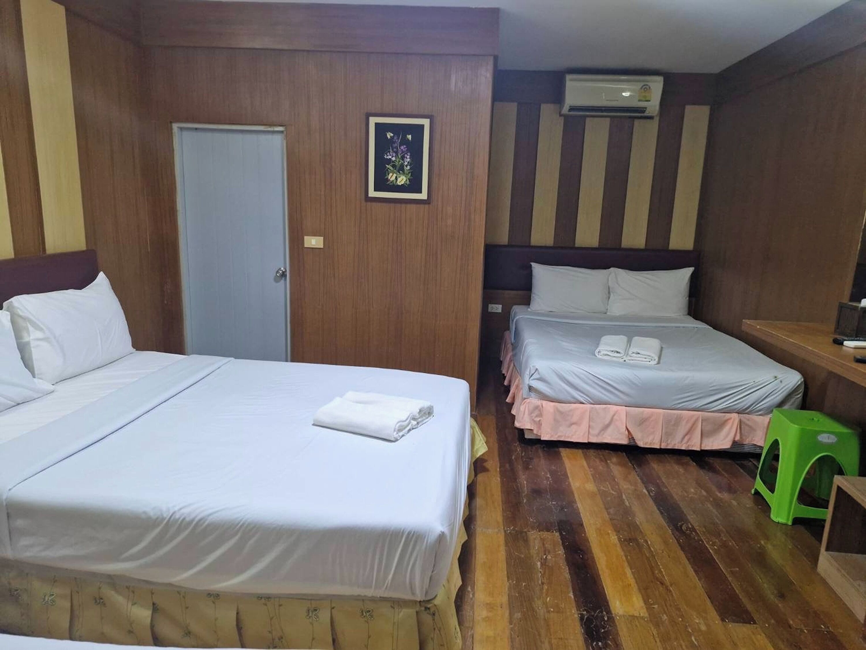 A hotel room with two beds, a wooden floor, a door, a framed picture, and an air conditioning unit.