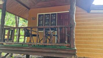 A wooden cabin with a porch, a door with glass panels, and a small outdoor seating area with chairs.