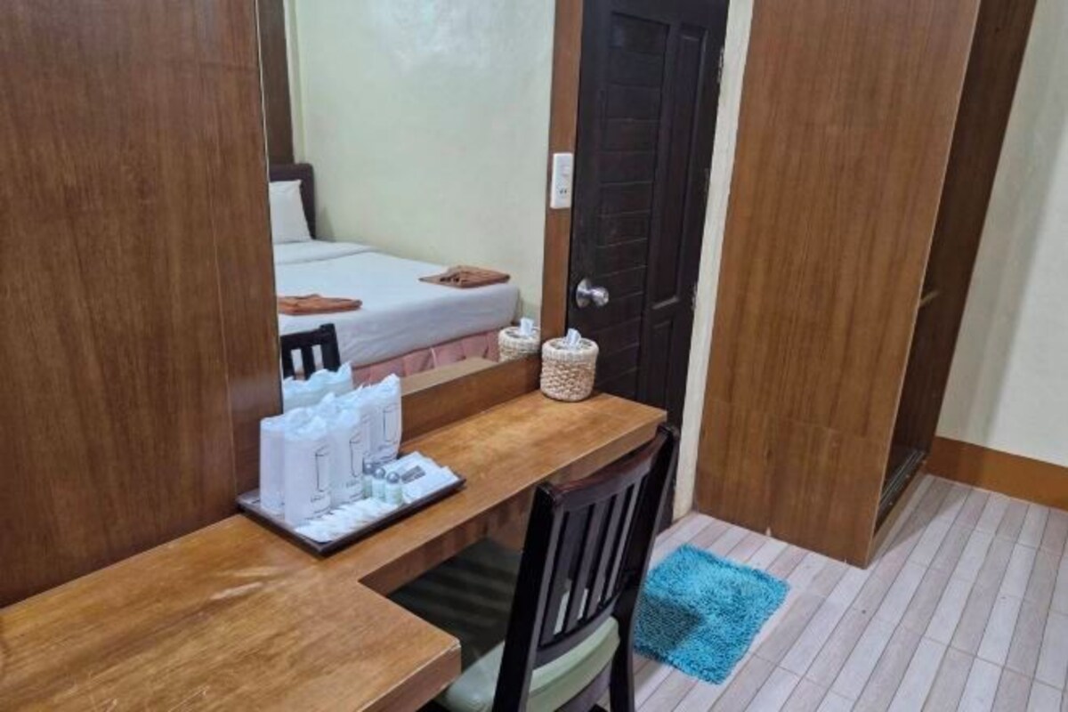 A small room with a wooden desk, a chair, a bed, and a blue rug.