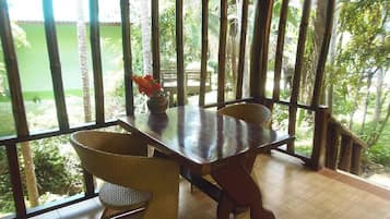 A dining area with a table and chairs, a vase with flowers, and a view of greenery outside.