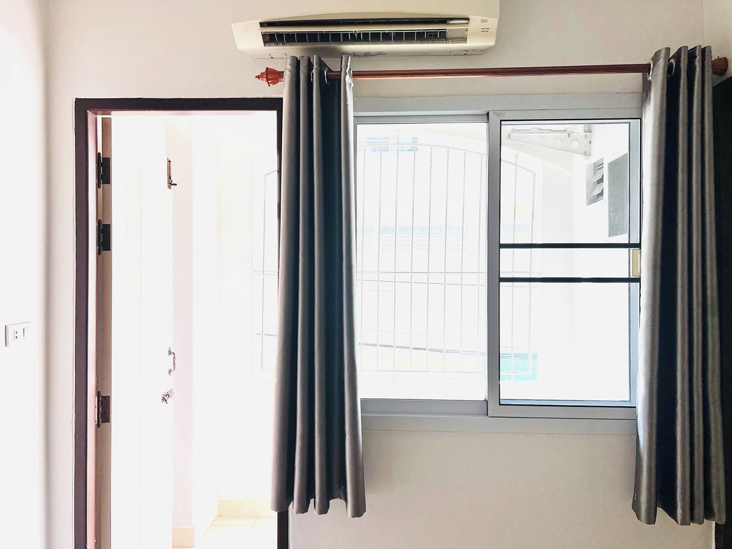 A room with a sliding glass door, a window with curtains, and an air conditioning unit above the window.