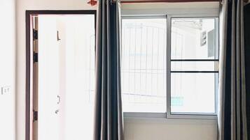 A room with a sliding glass door, a window with curtains, and an air conditioning unit above the window.