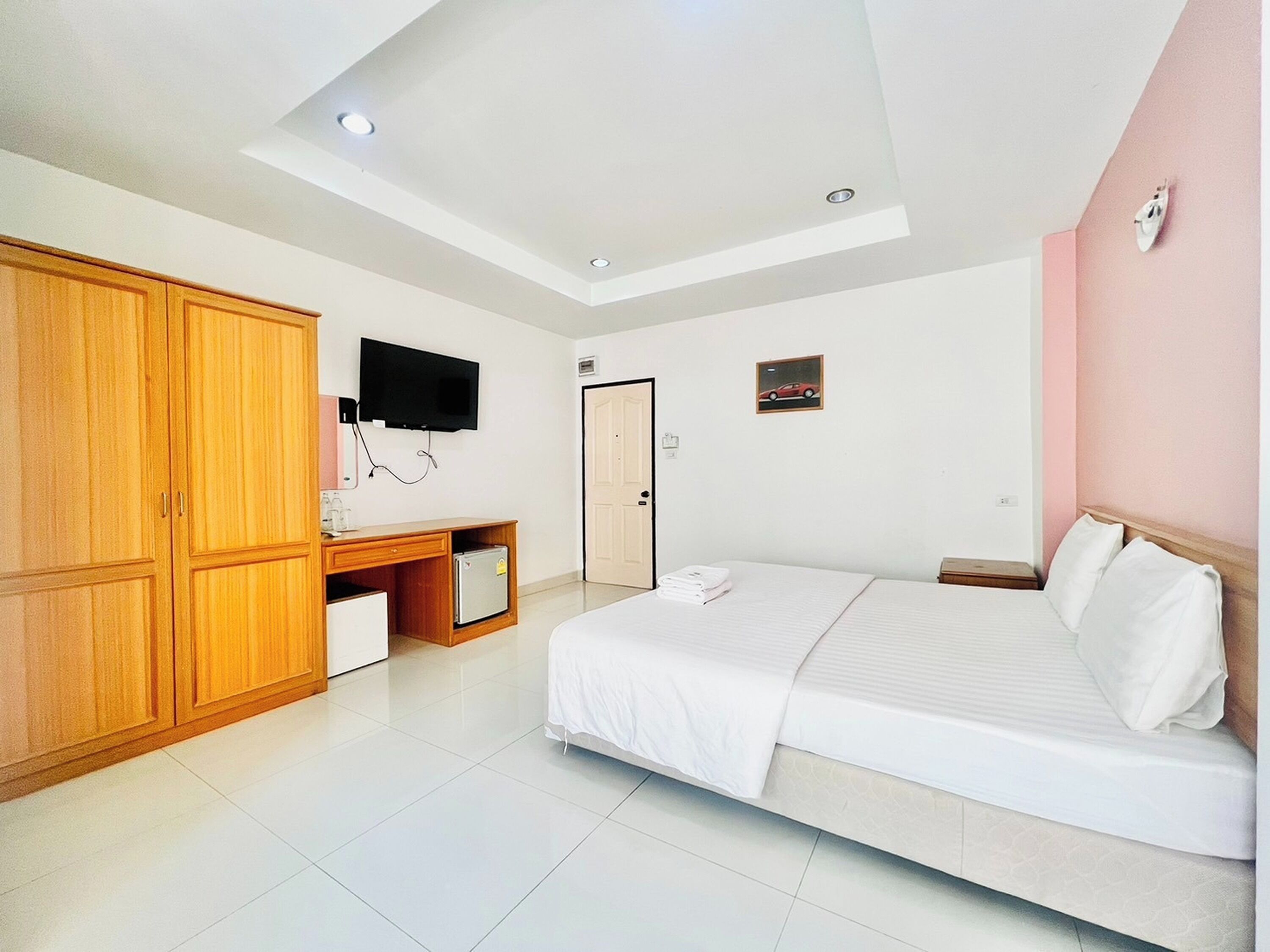 A bedroom with a bed, a wardrobe, a desk with a computer, a television, and a door.