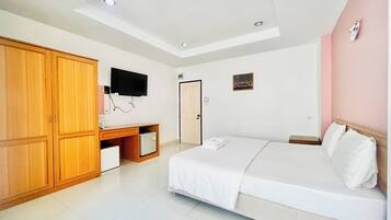 A bedroom with a bed, a wardrobe, a desk with a computer, a television, and a door.