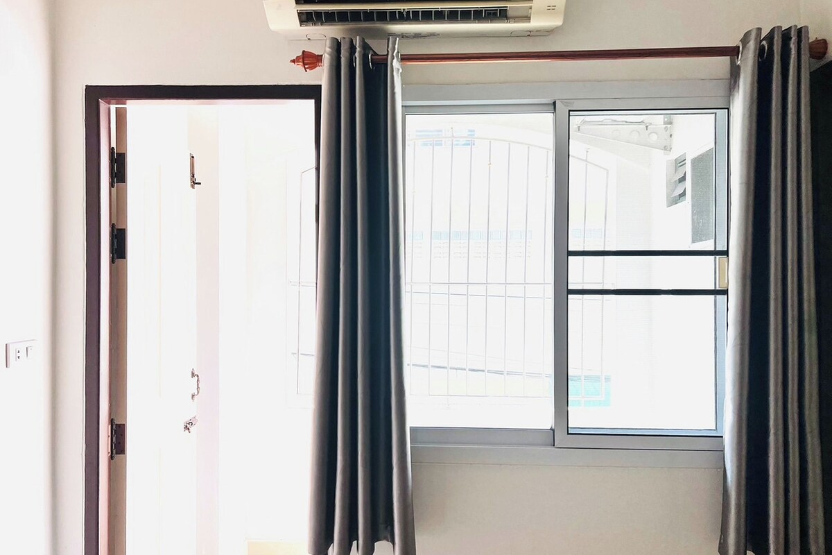A room with a sliding glass door, a window with curtains, and an air conditioning unit above the window.