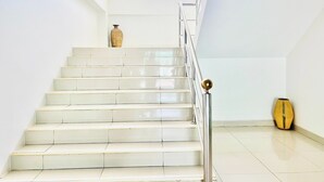 Eine Treppe mit weißen Stufen und einem Metallgeländer, die zu einer Zwischenebene mit einem kleinen Fenster führt.