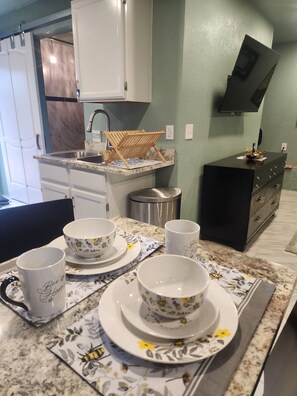 A kitchen with a sink, a wooden drying rack, a black cabinet, and a dining table set with floral-patterned plates and cups. - Mountain Chic Cabin Retreat (Woodland Park)