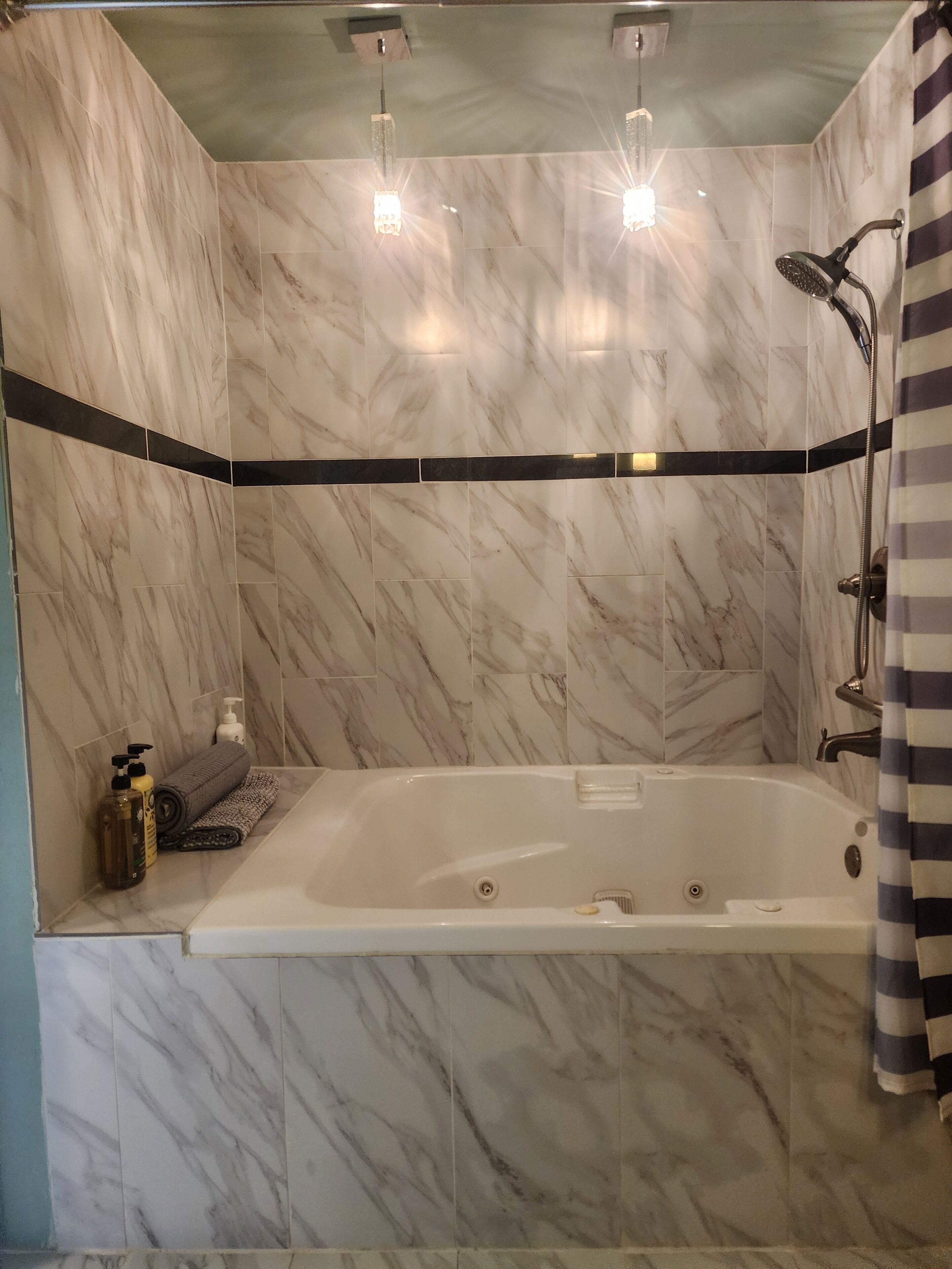 A bathroom with a marble wall, a bathtub, a shower, and a striped curtain.
