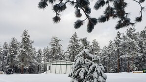 A snow-covered landscape with a small building and a snow-laden tree in the foreground. - Mountain Chic Cabin Retreat (Woodland Park)