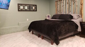 A bedroom with a bed, a wall-mounted TV, a framed mirror, and a wooden wall decoration. - Mountain Chic Cabin Retreat (Woodland Park)